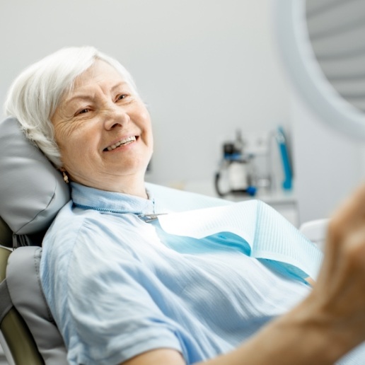 Senior woman in dental chair smiling in hand mirror