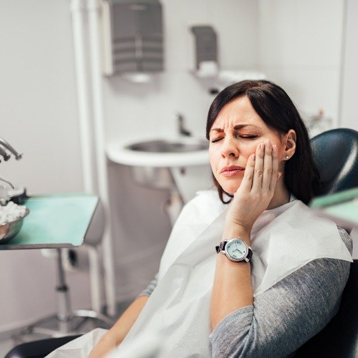 Woman in dental chair holding side of her face in pain