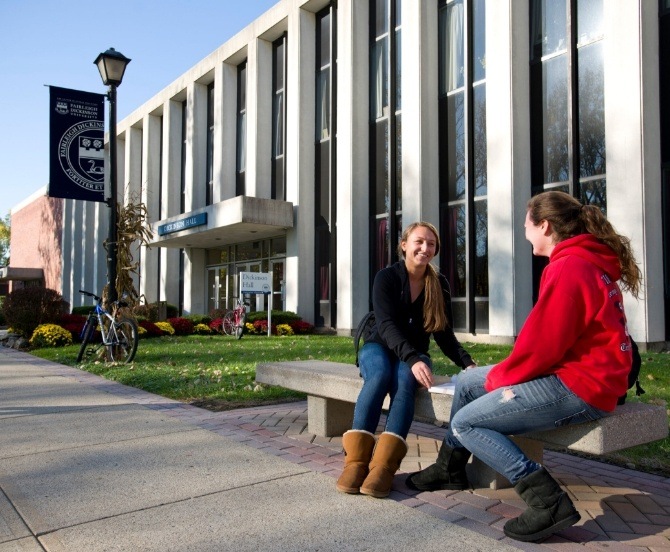 Two women sitting on bench outside of building at Fairleigh Dickinson University