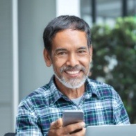 Smiling man in blue plaid shirt holding cell phone