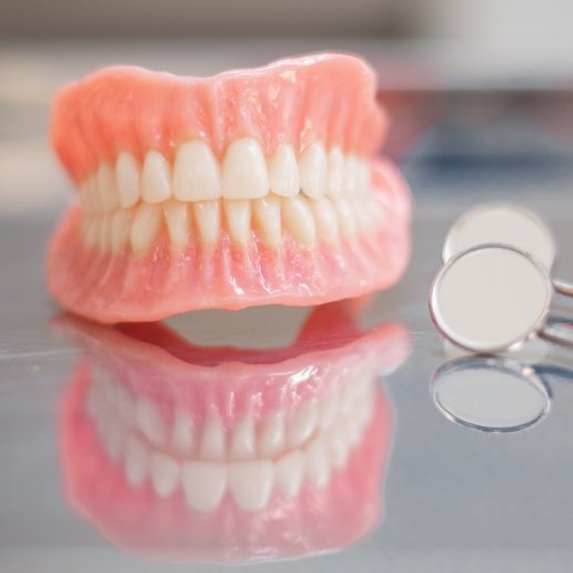 Set of full dentures in Chicago next to two dental mirrors
