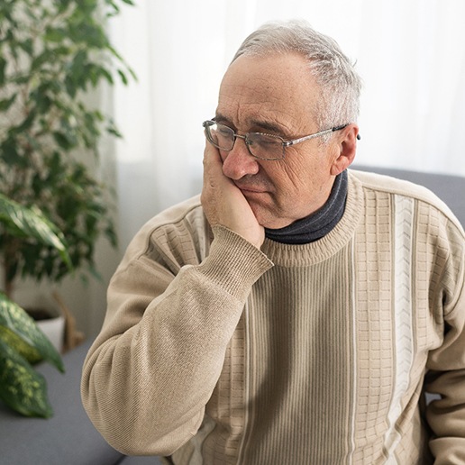 Older man in sweater sitting on couch and rubbing his jaw